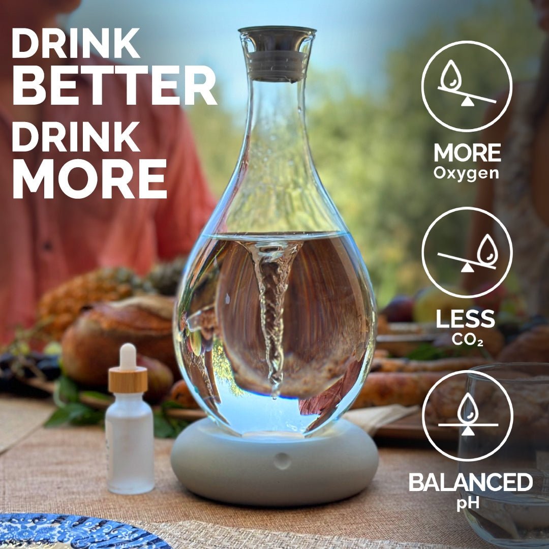 A Mayu Water Triple Swirl Bundle, crafted from handblown borosilicate glass, rests on a set table with a dropper bottle nearby. Text: Drink better—enjoy pH-balanced water with more oxygen and less CO₂. A person is blurred in the background.