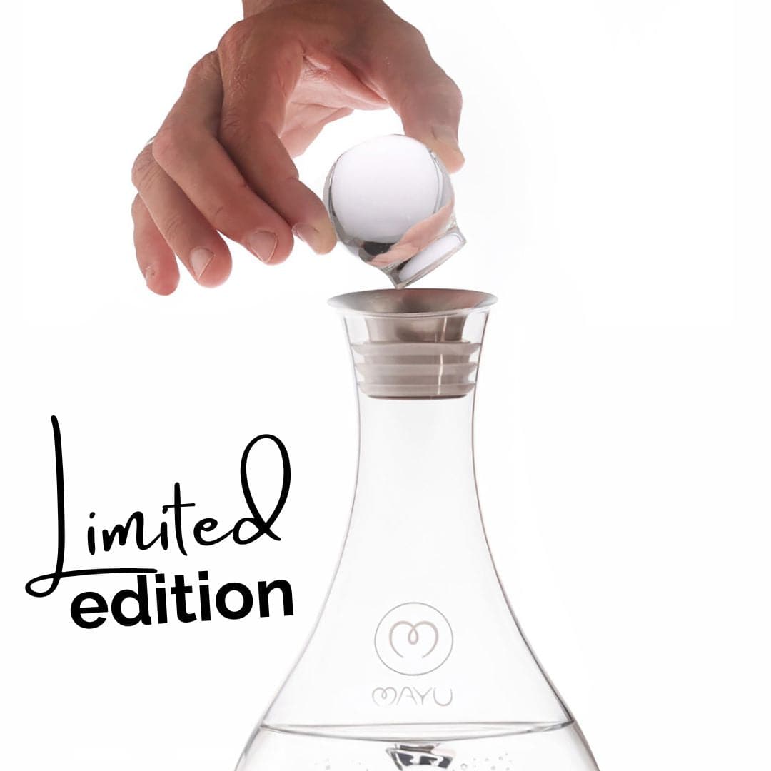 A hand drops a Limited Edition Glass Topper into a Swirl Water Carafe filled with water. Limited edition and the Mayu Water logo are displayed on the decanter.