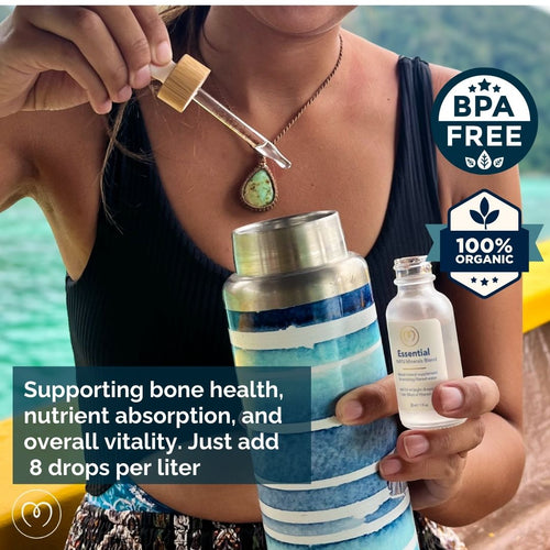 A person adds Mayu Water Trace Mineral & Electrolyte Drops Sampler Kit from a small bottle into a striped water bottle. The BPA-free, 100% organic drops support bone health, hydration, and vitality—add 8 drops per liter.