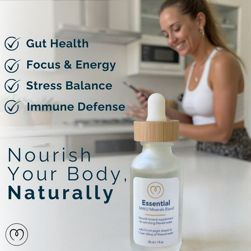 A smiling woman stands in a bright kitchen holding her phone. On the counter is the Mayu Water Trace Mineral & Electrolyte Drops Sampler Kit. Text highlights benefits: gut health, hydration, focus & energy, stress balance, and immune defense.