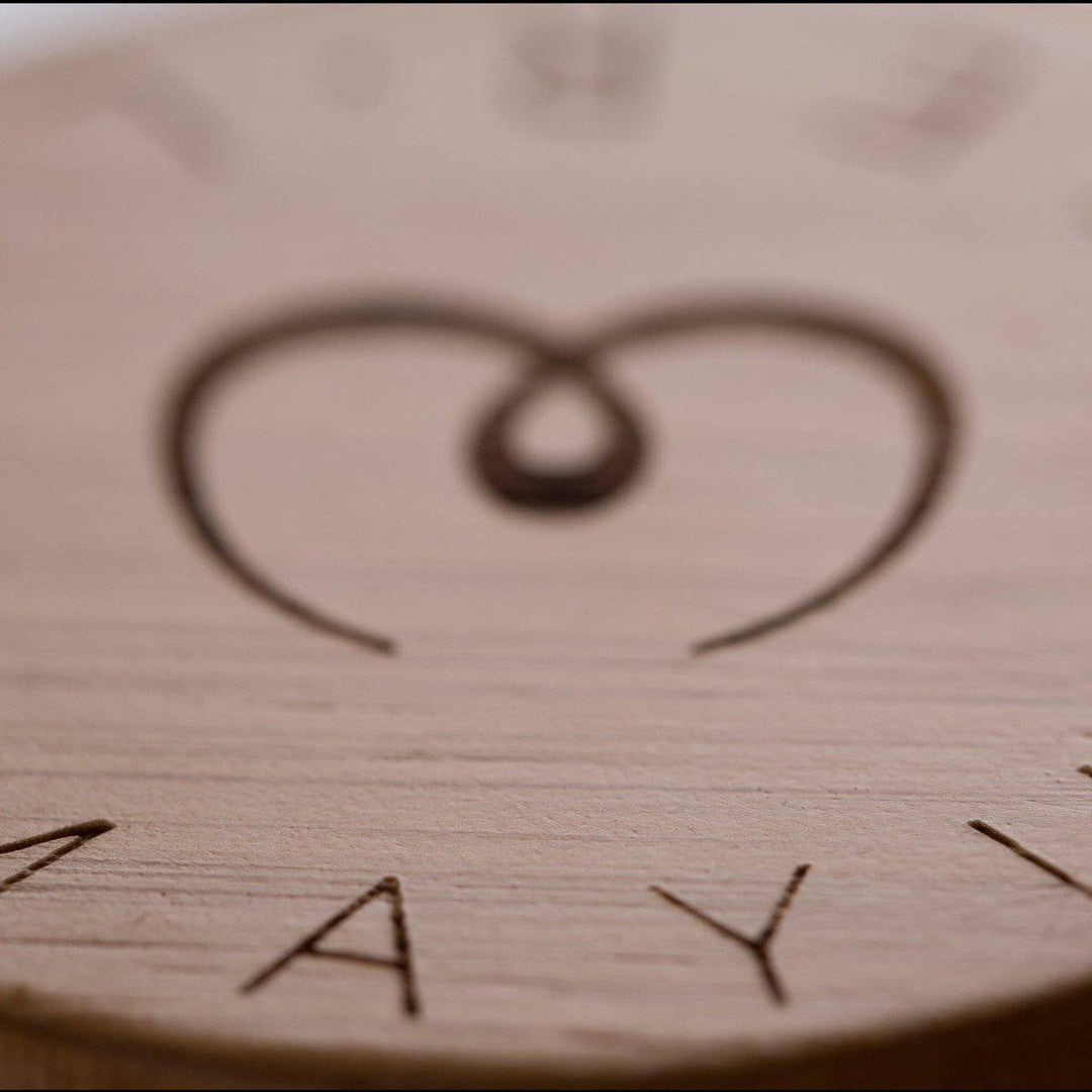 A close-up of a carved wooden surface with a heart and infinity symbol evokes the eco-friendly, minimalist charm of the Pure Glass Bottle by Mayu Water.