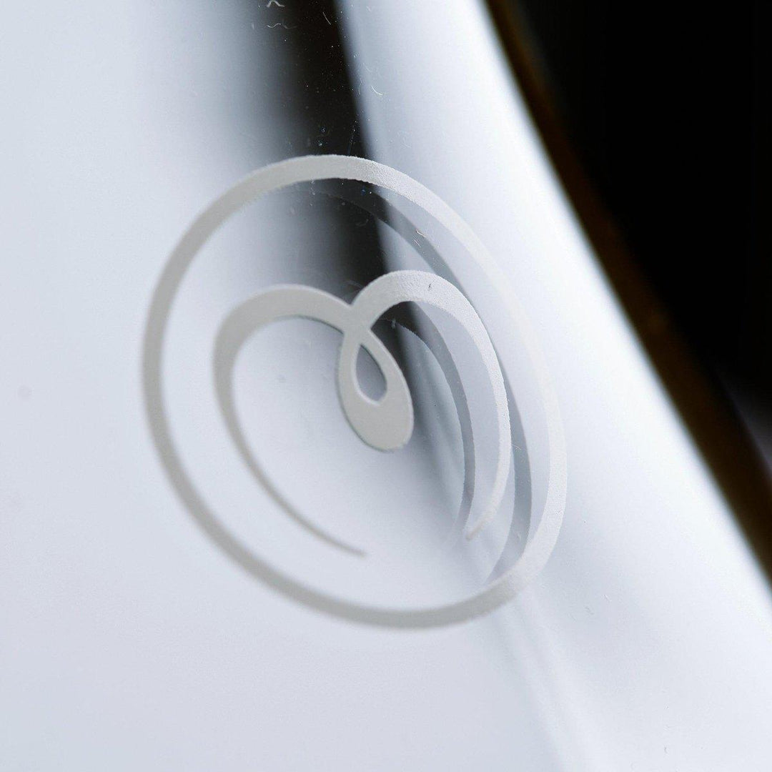Close-up of a stylized white heart-shaped ice cream swirl logo on the reflective Mayu Water Swirl Glass Carafe, crafted from borosilicate glass, set against a blurred background.