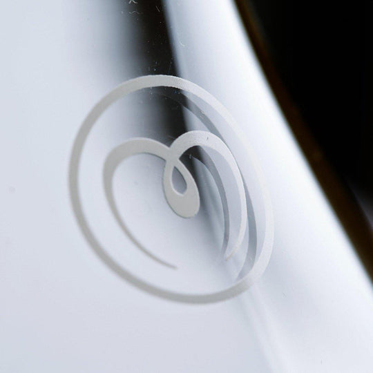 Close-up of a stylized white heart-shaped ice cream swirl logo on the reflective Mayu Water Swirl Glass Carafe, crafted from borosilicate glass, set against a blurred background.