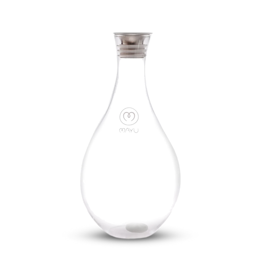 The Swirl Glass Carafe by Mayu Water is a clear, teardrop-shaped borosilicate glass carafe with a silver lid, a small white sphere at the bottom, and "MAYU" plus the logo on front, shown against a plain white background.