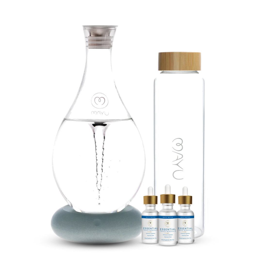 The Mayu Water Deluxe Starter Kit features a structured water carafe, a tall glass bottle with a wooden lid, and three trace mineral drop bottles, arranged on a white background to highlight optimal hydration.