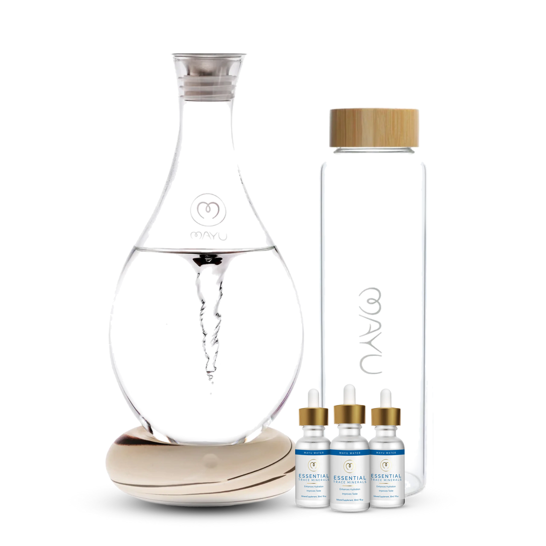 The Mayu Water Deluxe Starter Kit features a structured water carafe on a wooden base, a glass water bottle with bamboo lid, and three Essential Trace Mineral Drops, all displayed against a white background for optimal hydration.