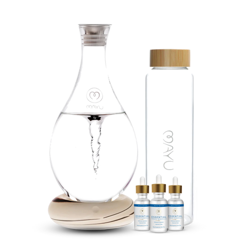 The Mayu Water Deluxe Starter Kit features a structured water carafe on a wooden base, a glass water bottle with bamboo lid, and three Essential Trace Mineral Drops, all displayed against a white background for optimal hydration.