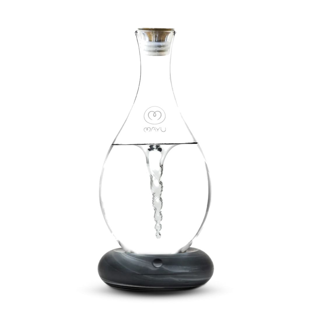 The Mayu Water Swirl Structured Water Carafe, with a lid and round dark base, creates a visible water vortex inside its clear glass body. The product is shown against a plain white background.
