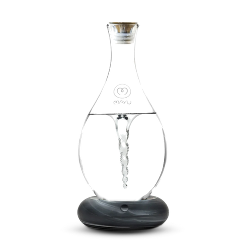The Mayu Water Swirl Structured Water Carafe, with a lid and round dark base, creates a visible water vortex inside its clear glass body. The product is shown against a plain white background.