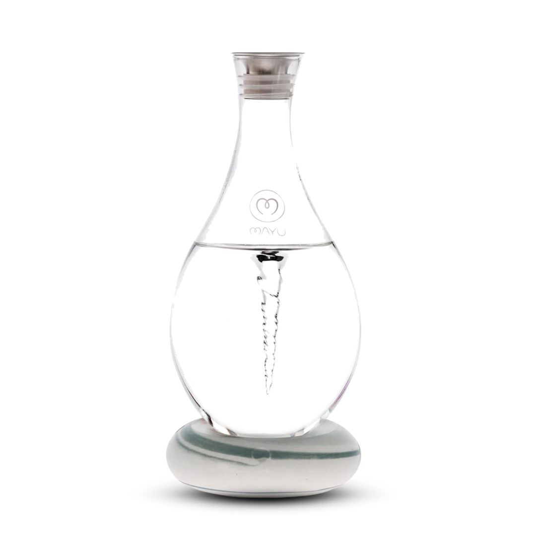 The Mayu Water Swirl Structured Water Carafe, featuring a spiral vortex design inside clear glass, sits on a round white base with a silver cap and branded logo, displayed against a plain white background.