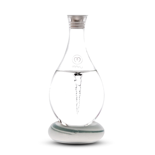 The Mayu Water Swirl Structured Water Carafe, featuring a spiral vortex design inside clear glass, sits on a round white base with a silver cap and branded logo, displayed against a plain white background.