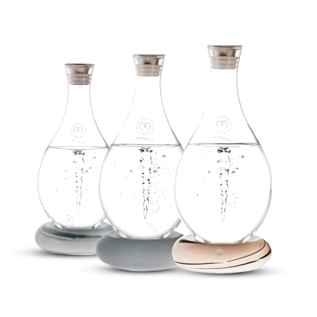 Three Swirl Structured Water Carafes by Mayu Water, each handblown from borosilicate glass with metal lids, rest on smooth stone-like bases. The pack of 3 features pH-balanced water with bubbles, set against a white background.