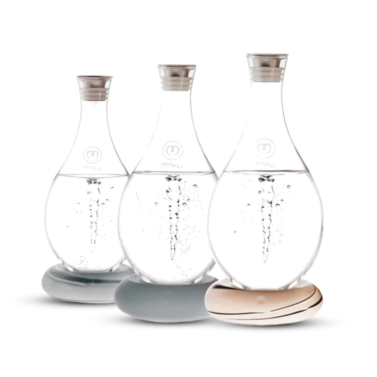 Three Swirl Structured Water Carafes by Mayu Water, each handblown from borosilicate glass with metal lids, rest on smooth stone-like bases. The pack of 3 features pH-balanced water with bubbles, set against a white background.