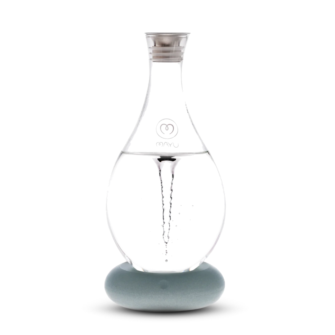 The Mayu Water Swirl Structured Water Carafe features a clear glass body with a pointed top on a round, light blue base. A visible water vortex swirls inside, all set against a white background.