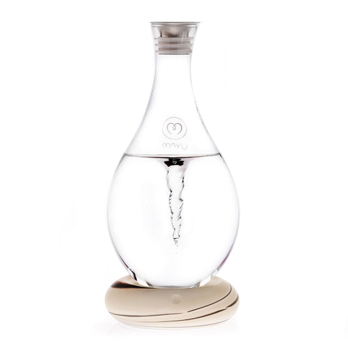 The MAYU Swirl Carafe by Mayu Water features clear glass with an internal spiral vortex, a narrow neck, silver cap, and sits on a smooth, light base. The front displays the "MAYU" brand name with a heart logo, designed to enhance your drinking water.