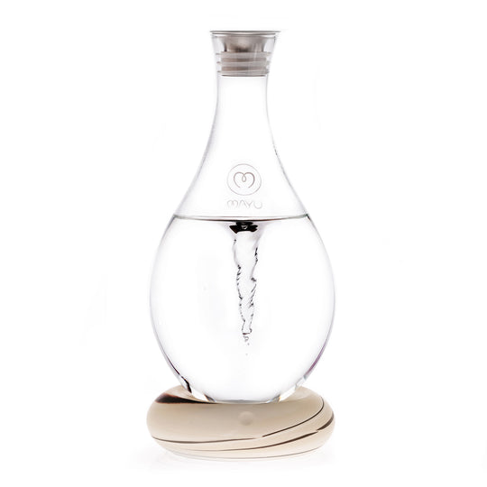 The MAYU Swirl Carafe by Mayu Water features clear glass with an internal spiral vortex, a narrow neck, silver cap, and sits on a smooth, light base. The front displays the "MAYU" brand name with a heart logo, designed to enhance your drinking water.