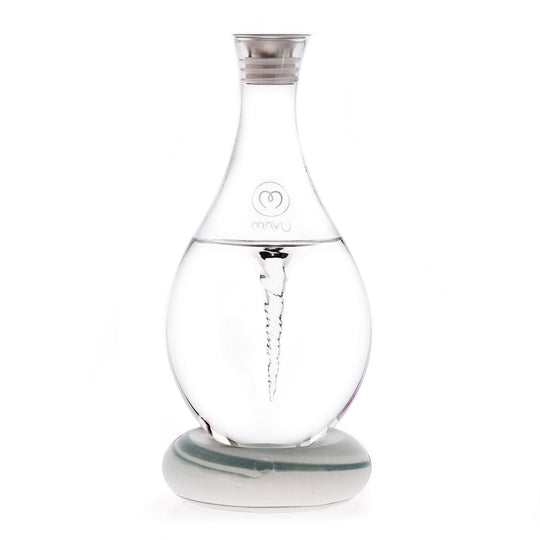 The MAYU Swirl Carafe by Mayu Water is a clear glass carafe with a silver cap on a round base. It creates a visible water vortex to enhance drinking water and features the MAYU logo on its front.