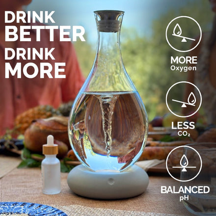 A Mayu Water Triple Swirl Bundle, crafted from handblown borosilicate glass, rests on a set table with a dropper bottle nearby. Text: Drink better—enjoy pH-balanced water with more oxygen and less CO₂. A person is blurred in the background.
