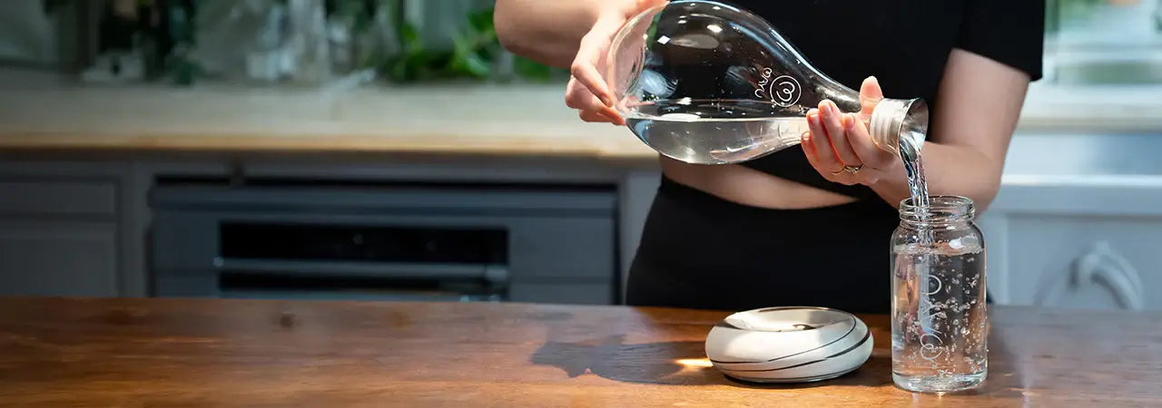 a woman pours water into a glass pitcher