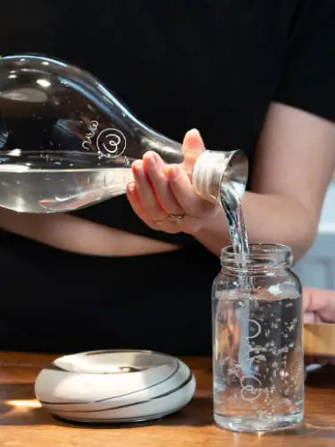 a person pouring water into a glass bottle